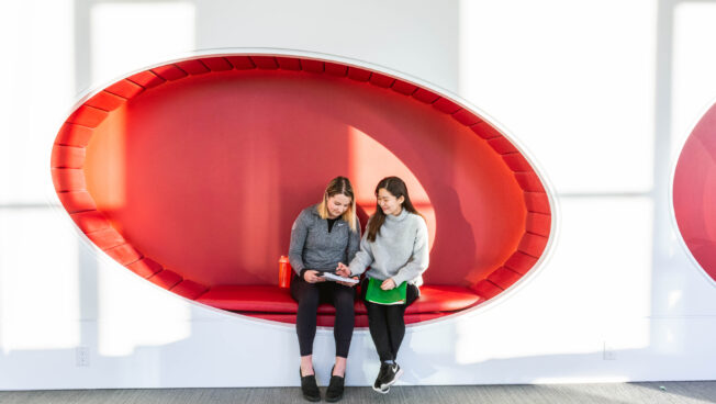 Two women discussing something in a notebook sitting in an interesting red booth