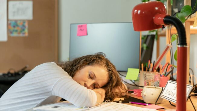 Student sitting at a desk surrounded by books and papers with unfinished assignments.