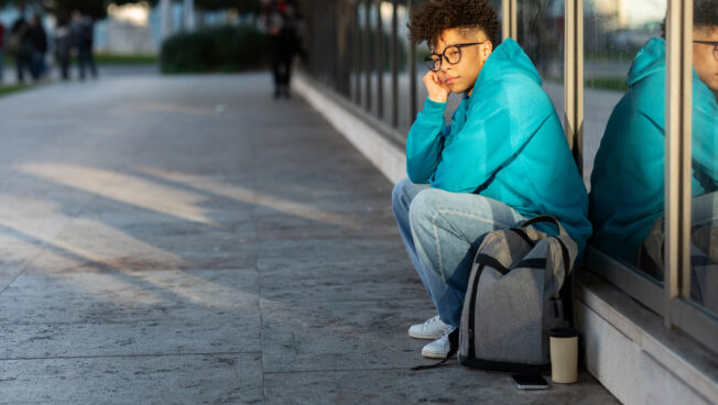 Unhappy student sitting with backpack at high school